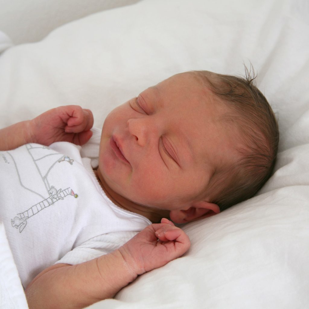 liggende baby tijdens fotoshoot onder een lakentje, hij lacht